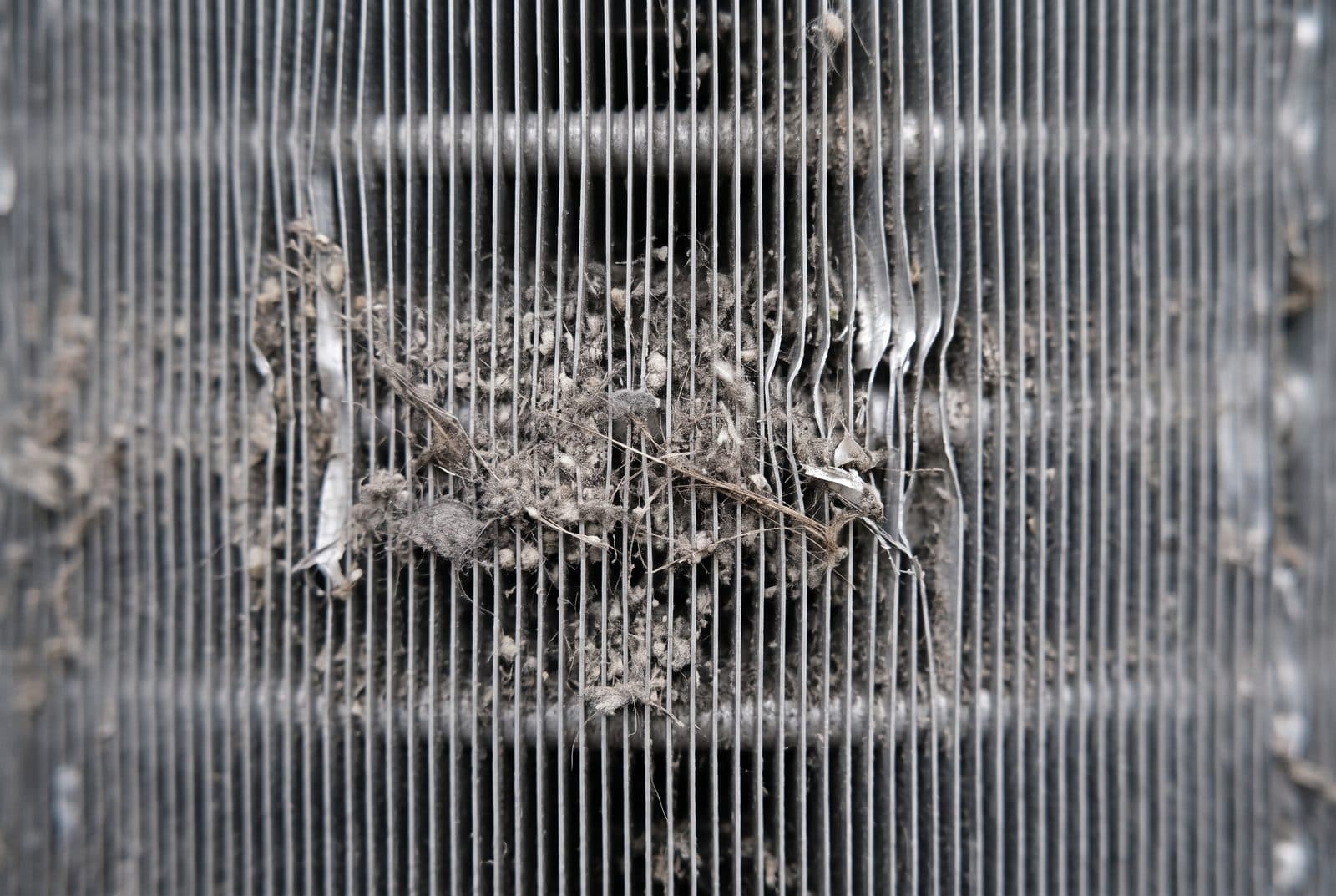 Gros plan sur les ailettes d'un échangeur de climatisation colmatées par la poussière et les peluches.