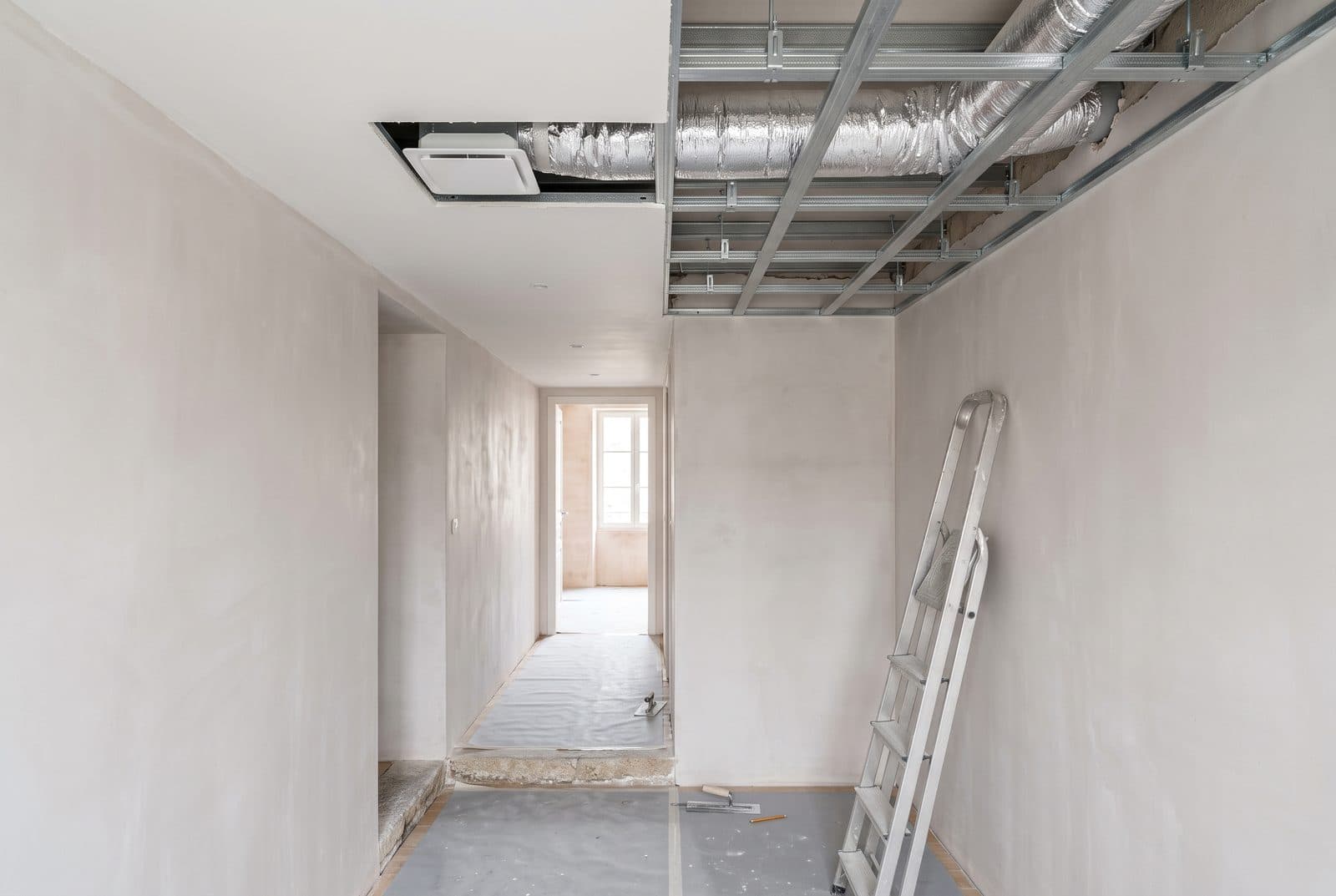 Couloir en travaux, faux plafond partiellement fermé laissant voir l'ossature métallique, une gaine isolée et une bouche déjà posée.