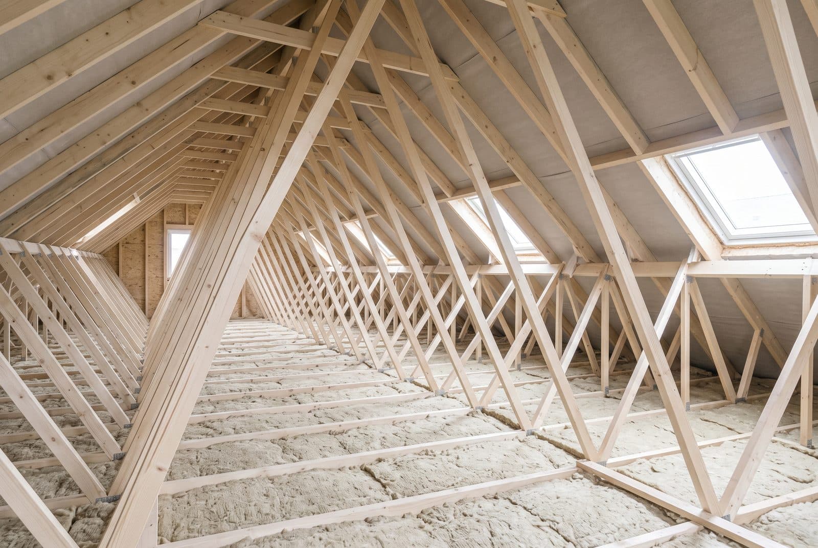 Combles perdus non aménagés d'une maison récente, traversés de part en part par une charpente à fermettes industrielles.