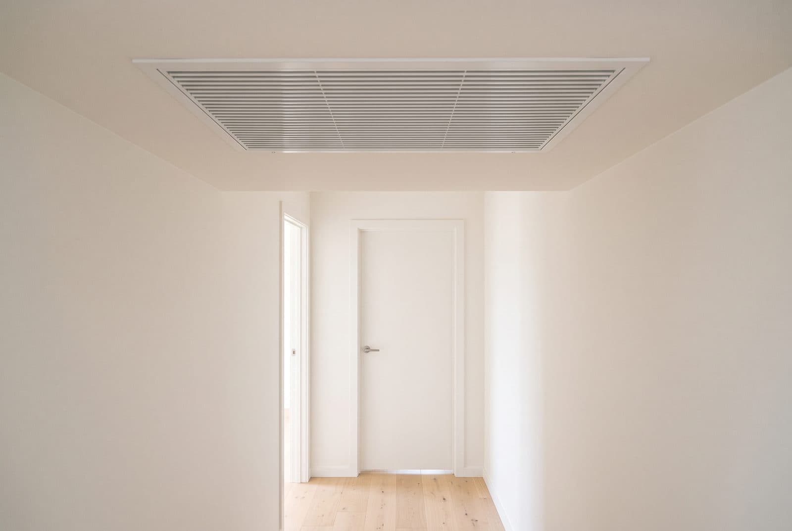 Grille de reprise d'air encastrée au plafond d'un couloir, et porte laissant un jeu au sol pour le passage de l'air.